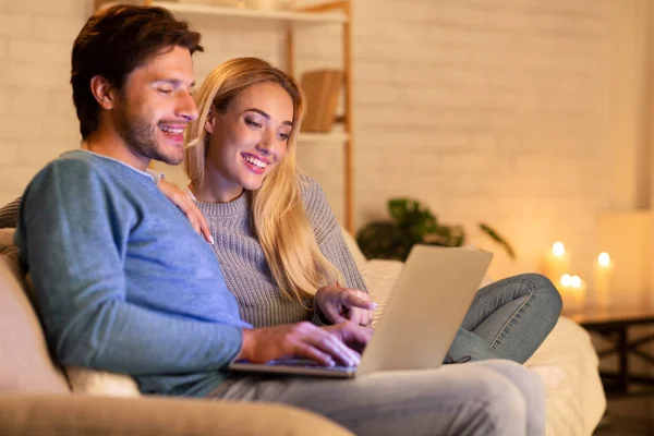 Улыбающиеся супруги, сидящие дома на диване с ноутбуком — стоковое фото