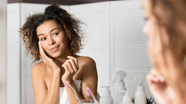 Young Lady Applying Cream Under Eyes Looking In Bathroom Mirror — Stok Foto