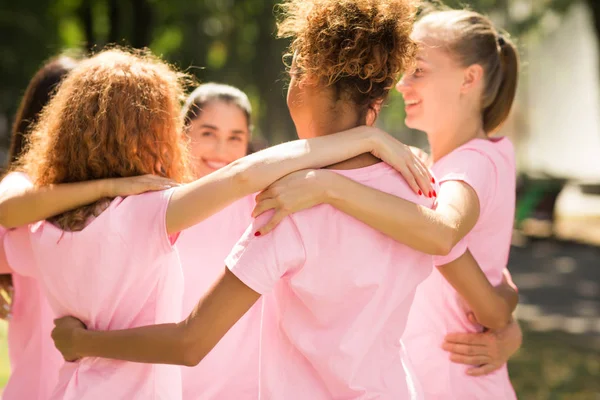 Multi-etnische meisjes in roze lint T-shirts knuffelen in cirkel buiten — Stockfoto