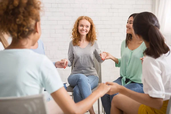 Diversas chicas sonriendo sosteniendo las manos sentadas en el interior — Foto de Stock