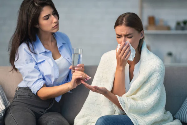 Mädchen gibt kranken Mitbewohnerin Pillen, die auf Couch im Haus sitzt — Stockfoto