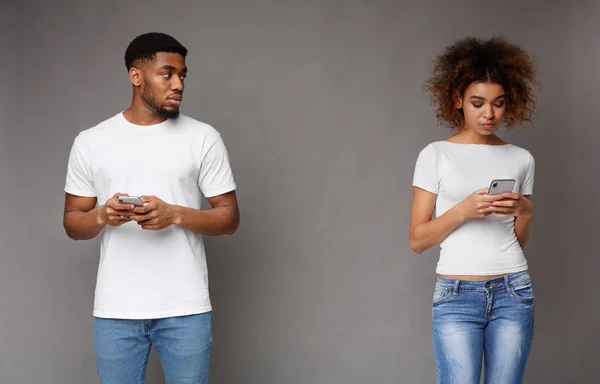 Triste homme noir regardant sa petite amie, femme concentrée textos au téléphone — Photo