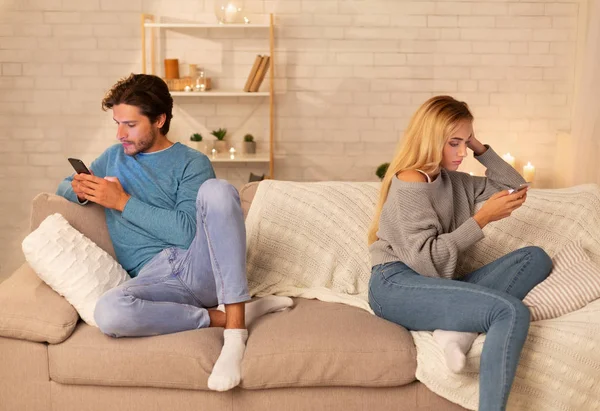 Couple indifférent utilisant des téléphones mobiles assis sur le canapé à la maison — Photo