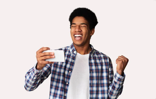 Веселий афро хлопець грає в ігри на мобільному телефоні — стокове фото