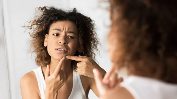 Afro menina espremendo espigão olhando no espelho no banheiro, panorama — Fotografia de Stock