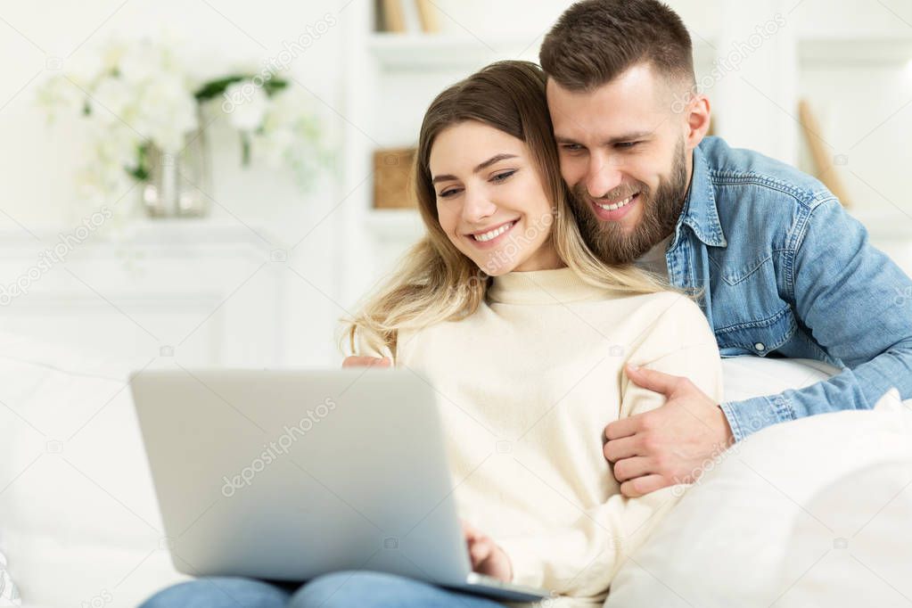 Beautiful young couple relaxing in living room and using laptop