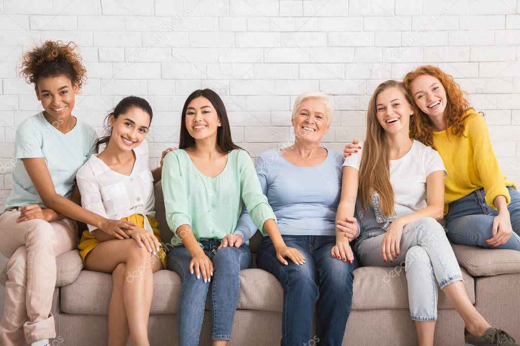 Group Of Women Smiling Sitting On Couch Against White Wall