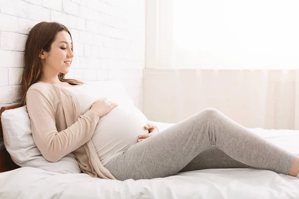 Jovem mulher grávida tocando sua barriga na cama — Fotografia de Stock