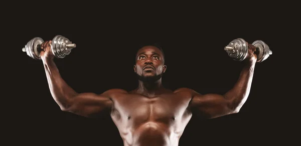 Konzentrierter schwarzer Bodybuilder beim Training, der die Hanteln nach oben schiebt — Stockfoto
