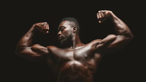 Athletisches afrikanisches Fitnessmodel lässt Muskeln über schwarzem Studiohintergrund spielen — Stockfoto