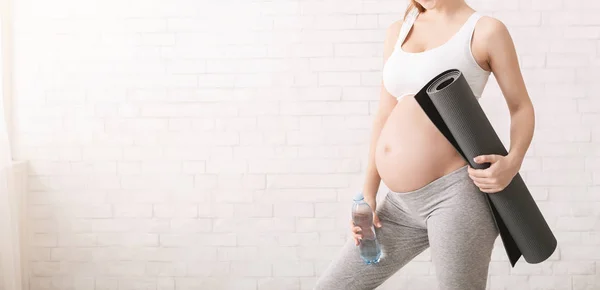 Mujer embarazada joven sosteniendo tapete de fitness y botella de agua — Foto de Stock