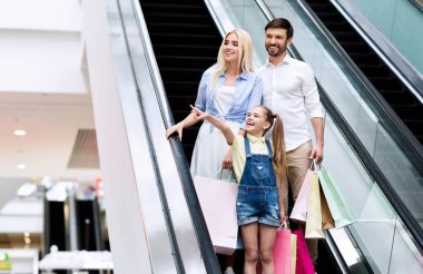 Kızı İşaret Parmak Alışveriş Merkezi'nde Ebeveynler ile Yürüyen Merdiven Üzerinde Ayakta