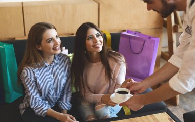 Garson alışverişten sonra kafede iki neşeli kız için kahve getirmek