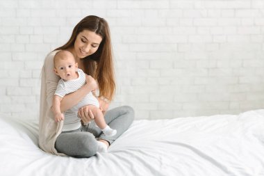 Genç gülümseyen anne elinde meraklı yeni doğan çocuk tutarak
