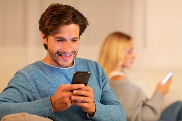 Ontrouw vriendje chatten op telefoon zittend met vriendin thuis — Stockfoto