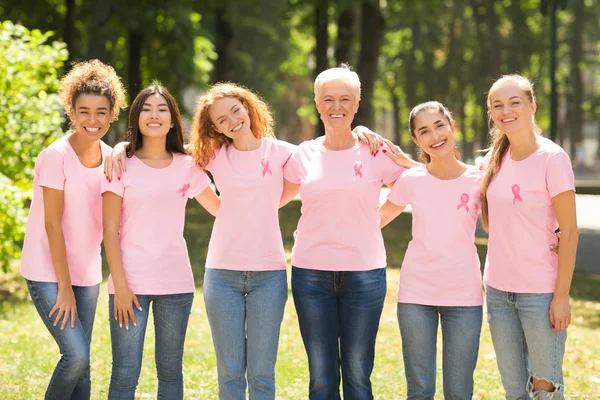 Senhoras multiétnicas em camisetas com fitas rosa abraçando no parque — Fotografia de Stock