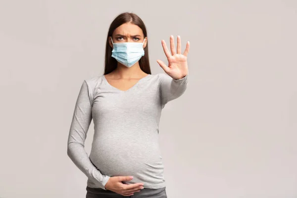 Zwangere vrouw in medische gezichtsmasker Gesturing stop, grijze achtergrond — Stockfoto