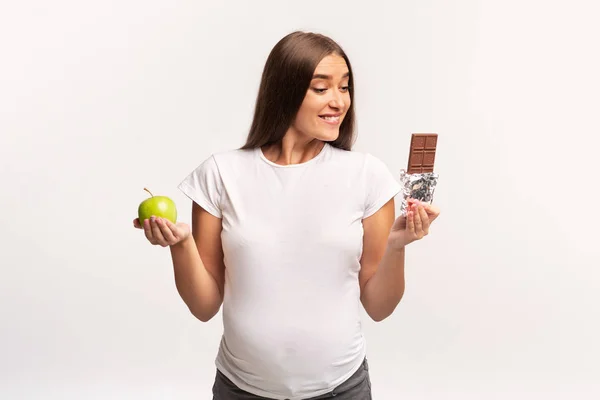 Pregnant Woman Choosing Between Apple And Chocolate, White Background