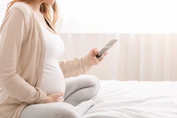 Terhes nő hálózatépítés a cellphone, ül az ágyban — Stock Fotó