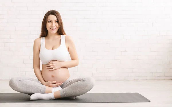 Активная беременная женщина прикасается к животу, отдыхает после тренировки — стоковое фото