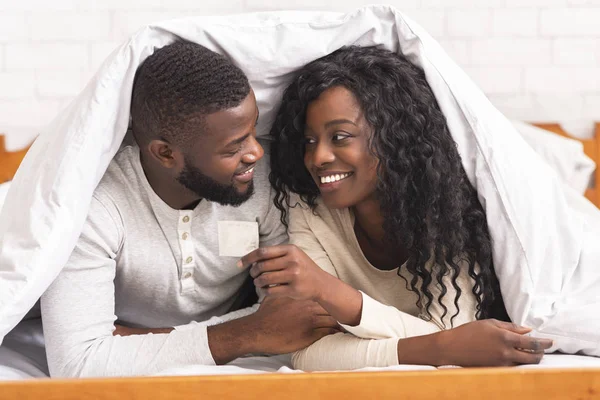 Schwarzes Paar mit Kondom im Bett unter weißer Decke — Stockfoto