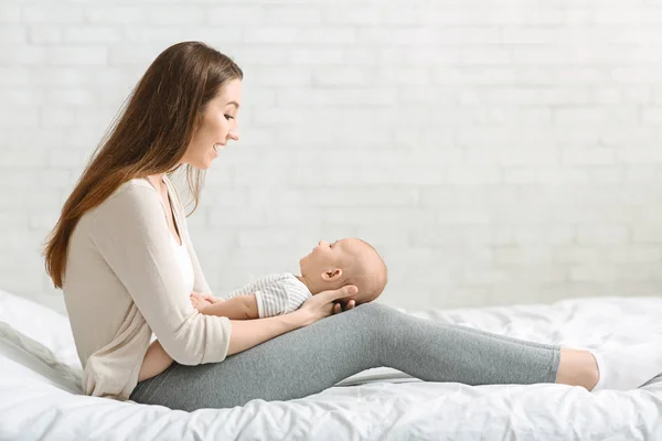 Glad mamma leker med sin bedårande lilla bebis i sängen — Stockfoto