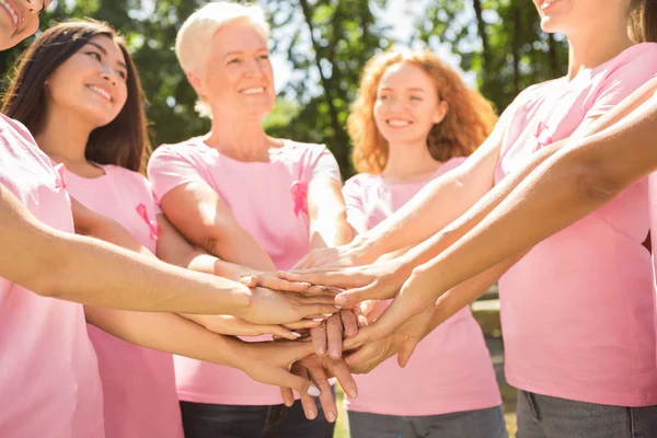 Diversos voluntarios en camisetas de cinta rosa sosteniendo las manos al aire libre — Foto de Stock
