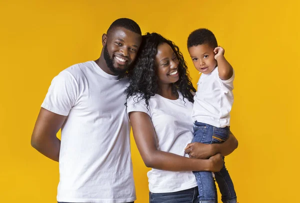 Feliz joven padres con lindo hijo sobre fondo amarillo — Foto de Stock