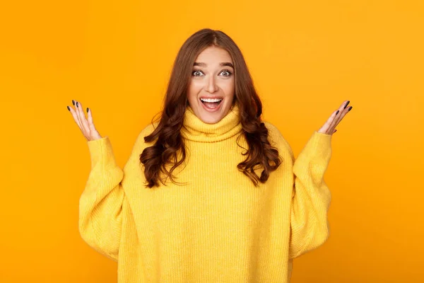 Excited woman raising hands in happiness, yellow background