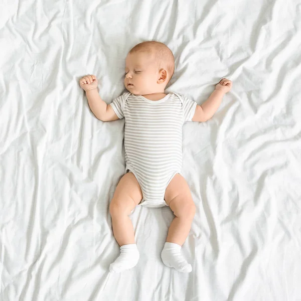 Adorable bebé recién nacido durmiendo en la cama con los brazos arriba —  Fotos de Stock