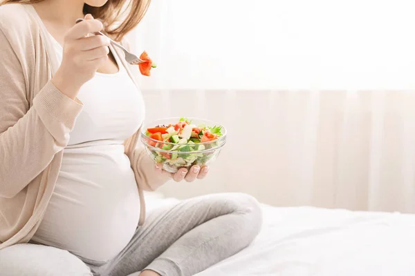 Беременная женщина ест свежий овощной салат в постели — стоковое фото