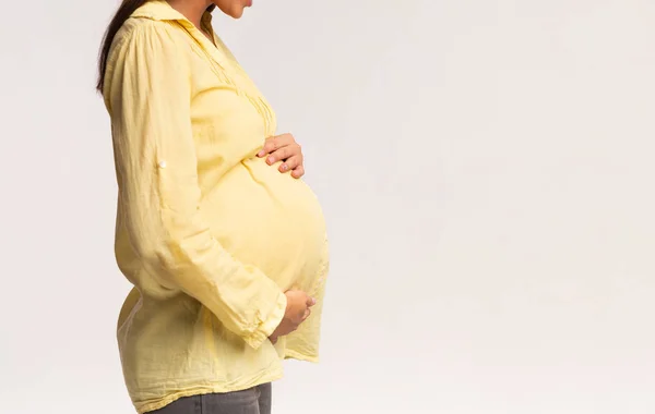 Неузнаваемая беременная женщина, стоящая на белом фоне, обрезанная, вид сбоку — стоковое фото