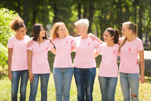 Mujeres multiétnicas en camisetas de cinta rosa abrazando al aire libre — Foto de Stock