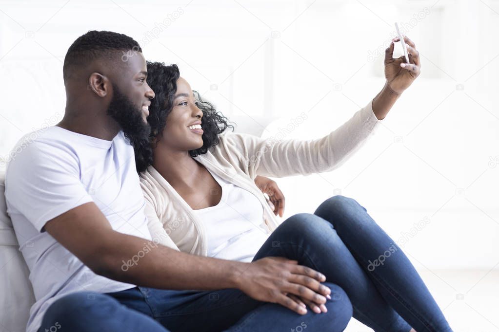 Black millennial couple taking selfie on smartphone at home