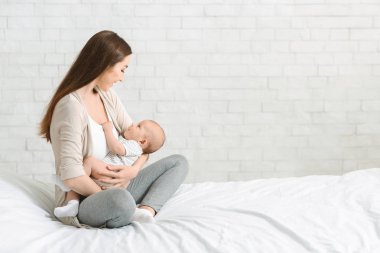 Genç gülümseyen anne yeni doğan çocuğuna hemşirelik