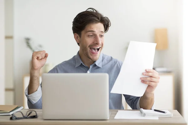 Uomo che celebra la vittoria seduto al computer portatile Holding Lettera sul posto di lavoro — Foto Stock