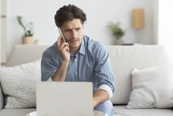 Cara tendo desagradável telefone conversa trabalhando no laptop em casa — Fotografia de Stock