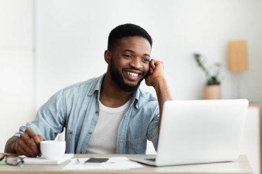 Dizüstü bilgisayarda çalışırken telefonda konuşan genç çalışan