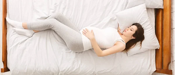 Vermoeide zwangere vrouw die in bed rust en haar buik aanraakt — Stockfoto