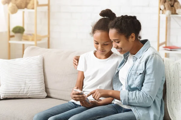 Twee schattige zusters met behulp van smartphone op de Bank thuis — Stockfoto