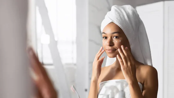 Mujer afroamericana aplicando crema para los ojos de pie cerca del espejo, Panorama — Foto de Stock