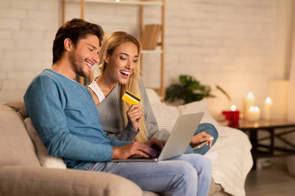Cónyuges felices usando el ordenador portátil y la tarjeta de compras en línea en casa —  Fotos de Stock