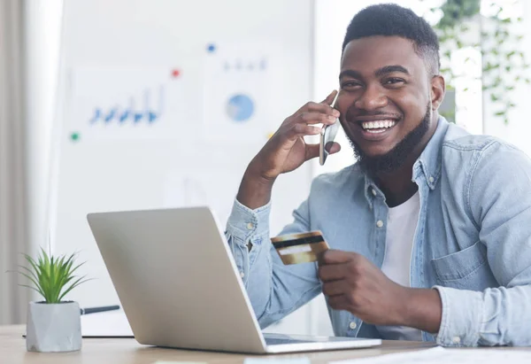 Allegro ragazzo nero che parla al telefono e tiene in mano la carta di credito — Foto Stock