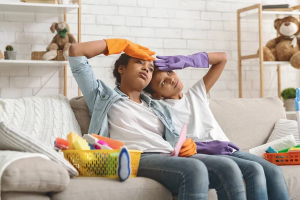 Vermoeide Afrikaanse zussen met schoonmaak handschoenen op de bank zitten — Stockfoto