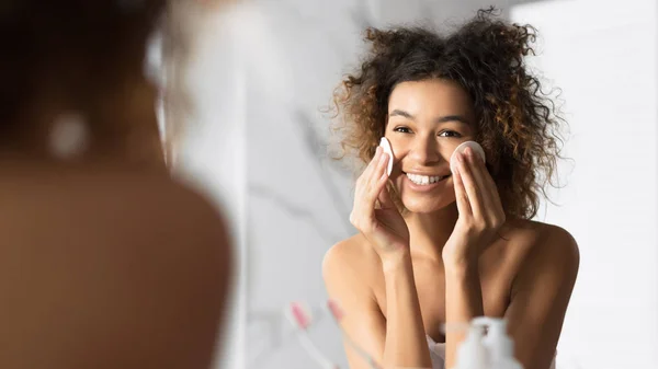 Афро-американская девушка держит хлопчатобумажные прокладки очищающее лицо в ванной комнате — стоковое фото