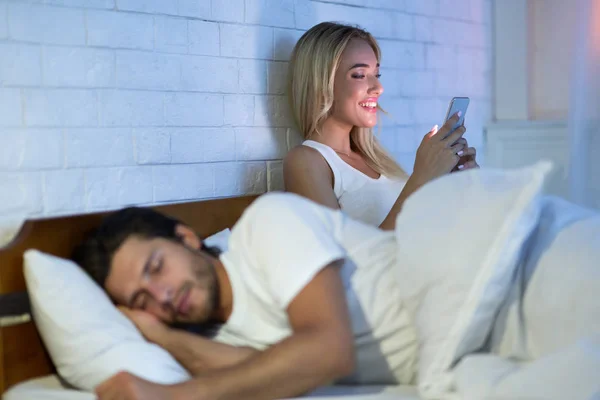 Batota mulher bate papo no celular enquanto marido dormindo no quarto — Fotografia de Stock