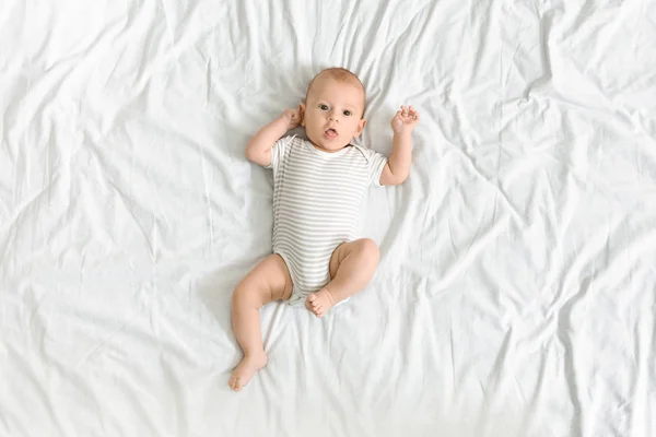 Lindo bebé en traje de cuerpo acostado en la cama, mirando a la cámara —  Fotos de Stock