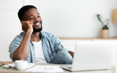 Handsome black man talking on phone while sitting at workplace