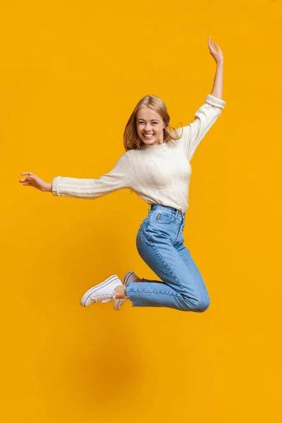 Дівчина-підліток весело стрибає в повітрі на помаранчевому фоні — стокове фото