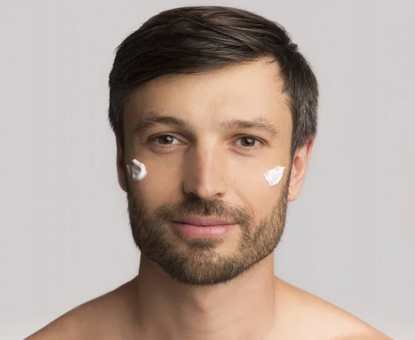 Homme mûr appliquant la crème visage sur la peau, fond blanc — Photo